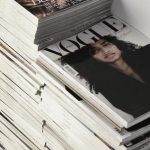 Nyc Style Trends: Dominating - High angle many fashion magazines stacked on floor against white brick wall in studio