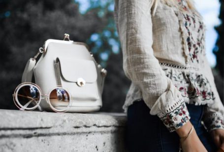 Style Trends - woman wearing beige and red floral top leaning on gray concrete slab with white leather bag ontop